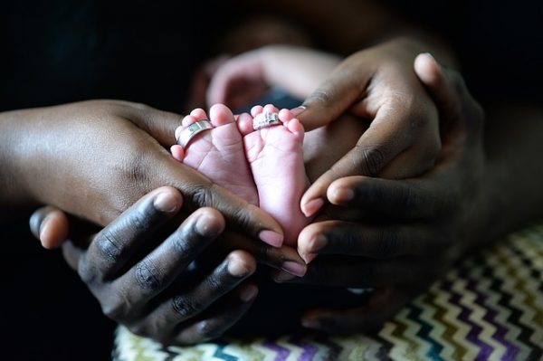 two pairs of hands cup a baby's feet. all three are different skin tones